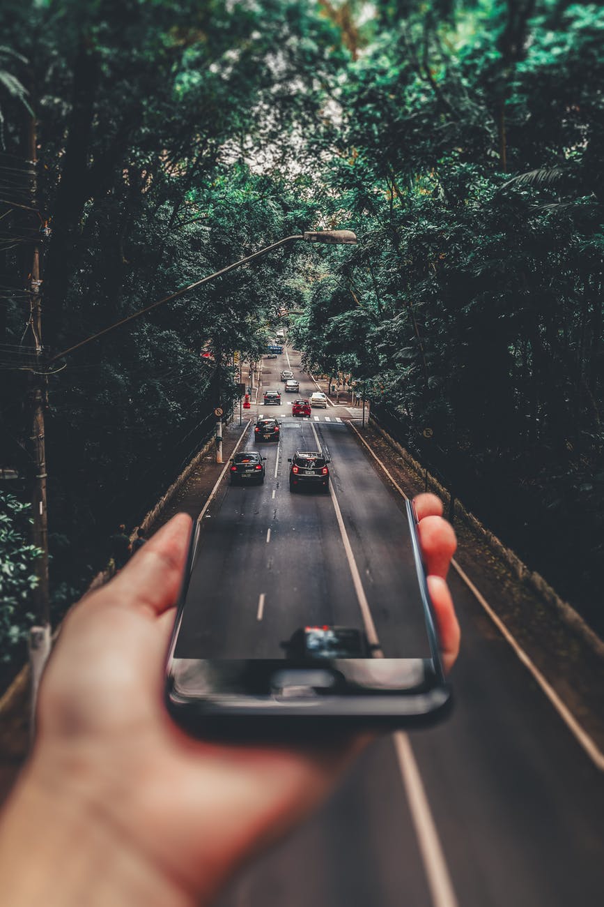 forced perspective photography of cars running on road below smartphone