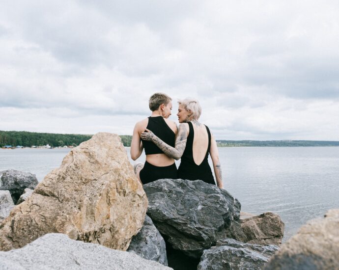 photo of women sitting on rocks near sea